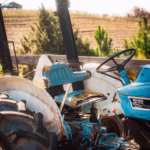 A rustic blue tractor sits idle against a picturesque farmland backdrop, evoking rural charm.