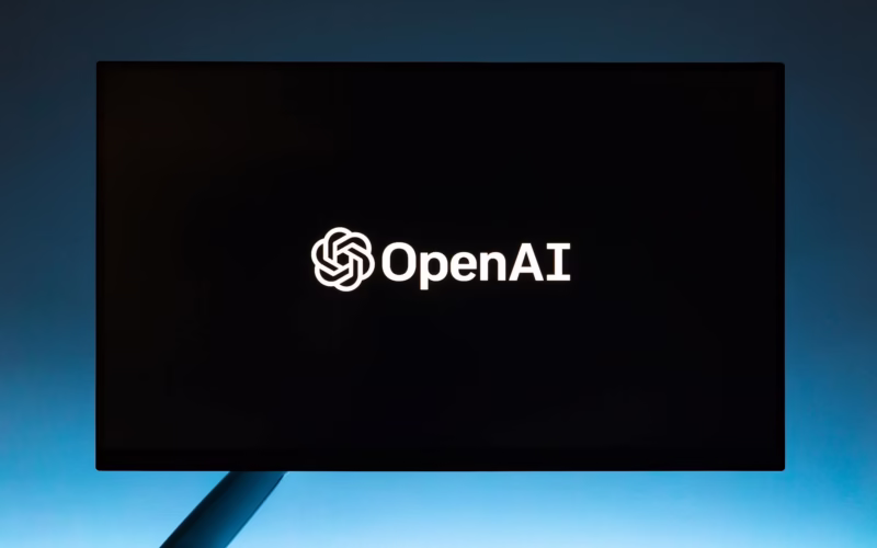 Minimalist display of OpenAI logo on a screen, set against a gradient blue background.