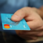 A close-up shot of a hand offering a blue debit card for payment.