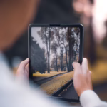 Person using tablet to capture and focus on a scenic pathway lined with trees outdoors.