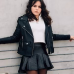 Young woman leaning on fence in stylish black leather jacket, exuding confidence.