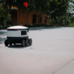A sleek autonomous food delivery robot navigates a sunny urban landscape, showcasing modern innovation.