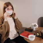 A woman sitting indoors, adjusting her face mask, symbolizing pandemic protection.