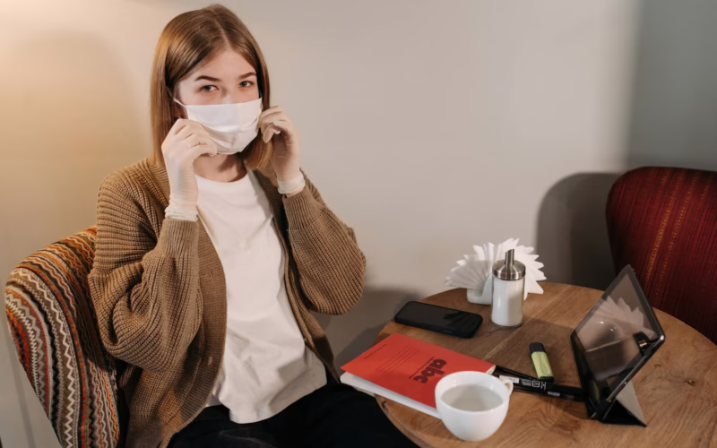 A woman sitting indoors, adjusting her face mask, symbolizing pandemic protection.