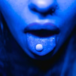 Dramatic close-up of a person with a tablet on their tongue in blue lighting.