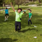Kids having fun outdoors at summer camp playing with paper airplanes.
