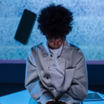 A teenager sits in a conceptual setting with a phone floating nearby.